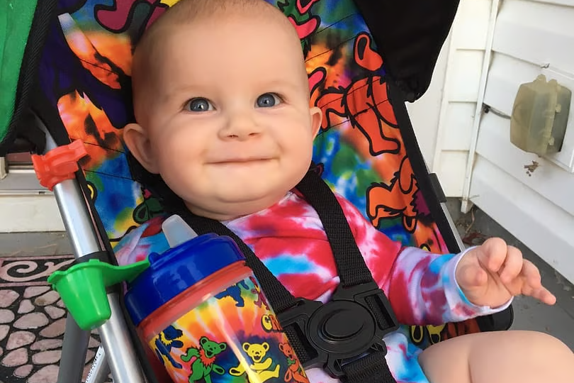 A photo of a cute baby in a tie dye onesie with a Daphyls Grateful Dead sippy cup. The baby is in a Daphyls brand Grateful Dead stroller.